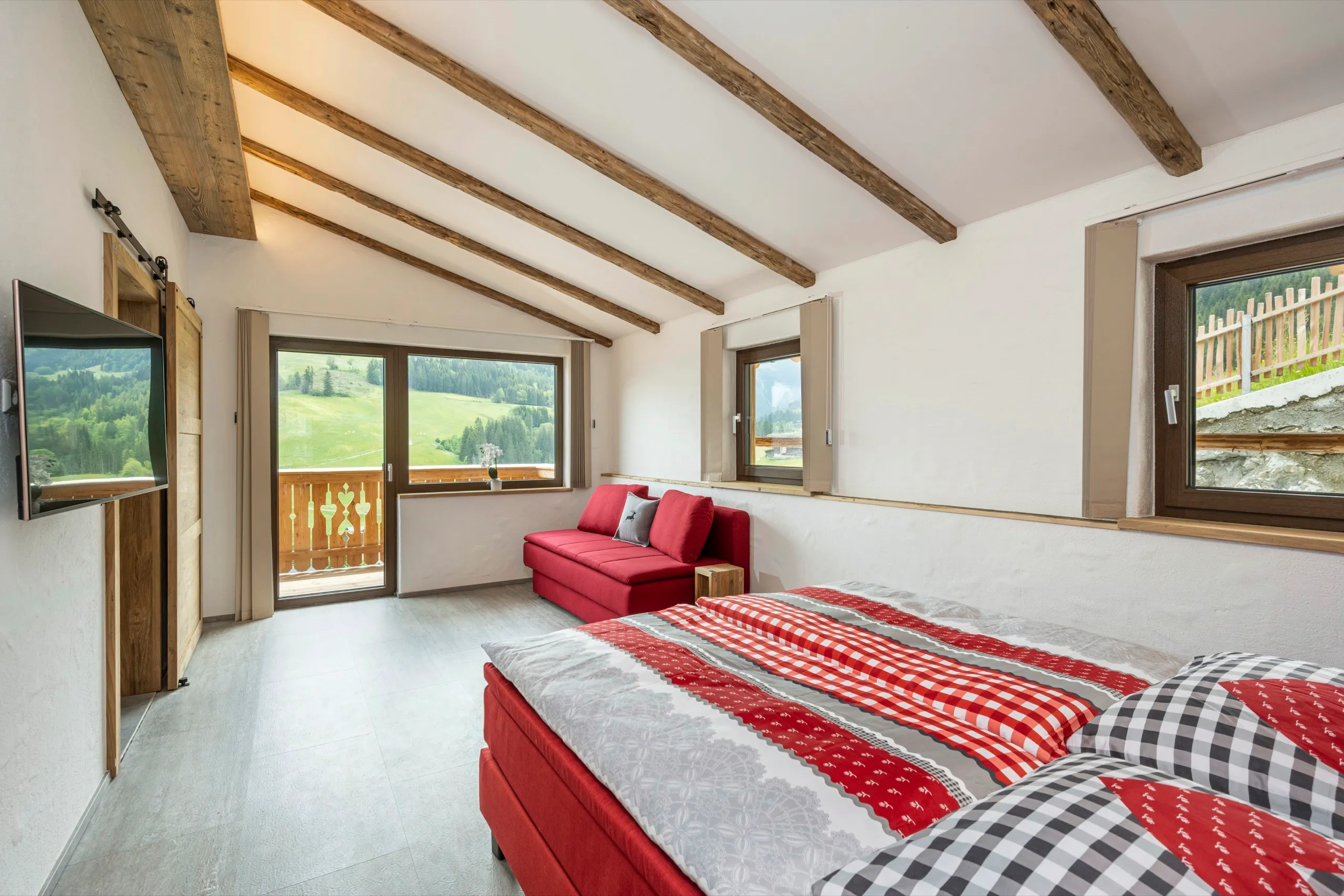 Schlafzimmer mit Doppelbett unter der Dachschräge, dahinter der Balkon
