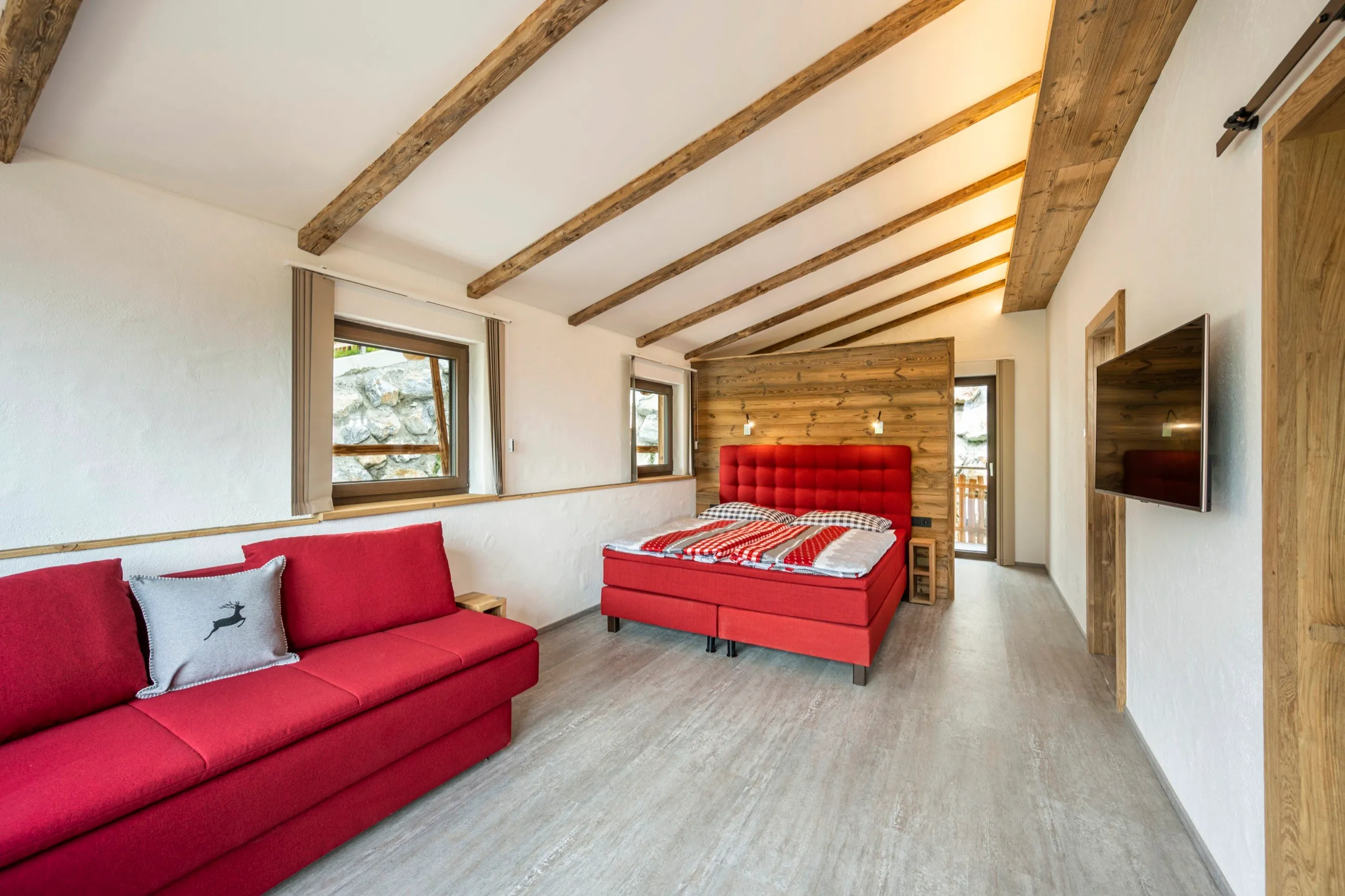 Schlafzimmer mit rotem Sofa und Doppelbett unter Holzbalken