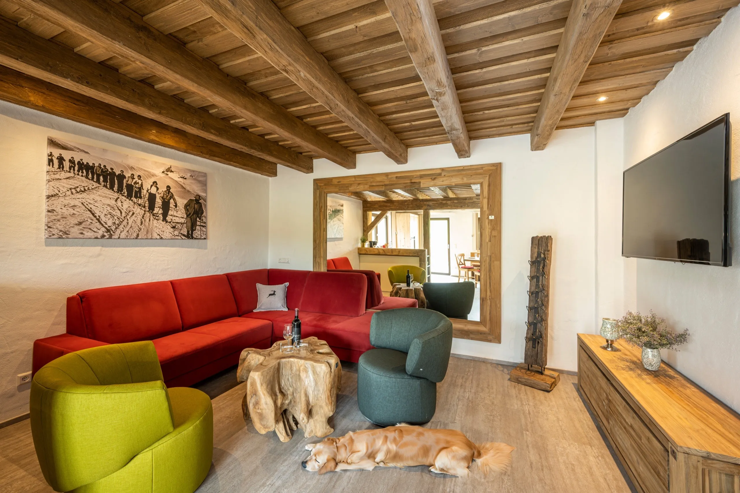 Wohnzimmer mit rotem Ecksofa unter der Holzdecke, davor liegt ein Hund